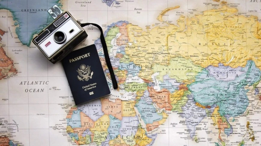 Widok z góry na mapę świata, na niej paszport i stary aparat.