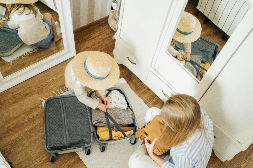 Kobieta i dziecko pakują walizkę, siedzą na podłodze koło szafy.